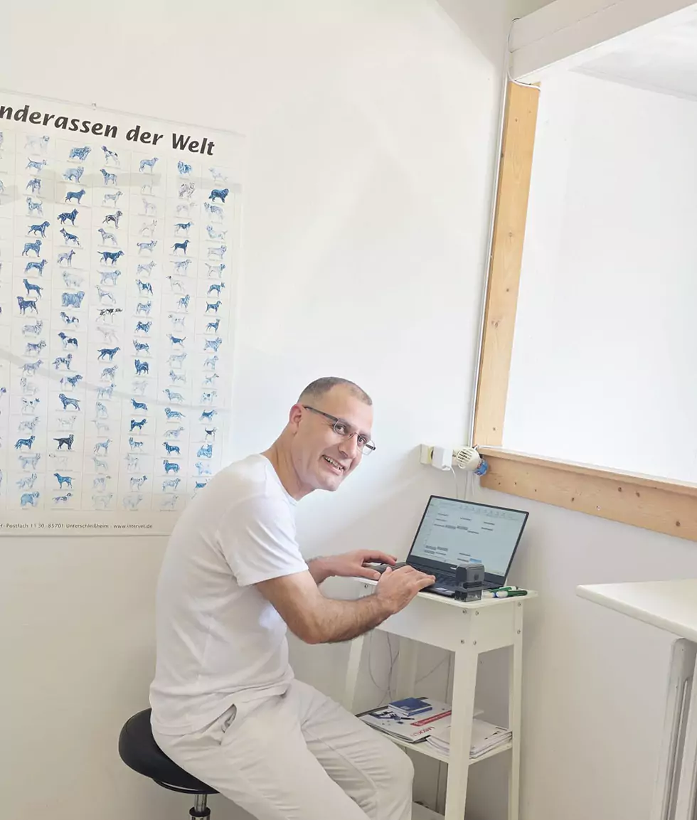 Dr. Emad Merey sitzt an seinem Laptop und lächelt freundlich in die Kamera